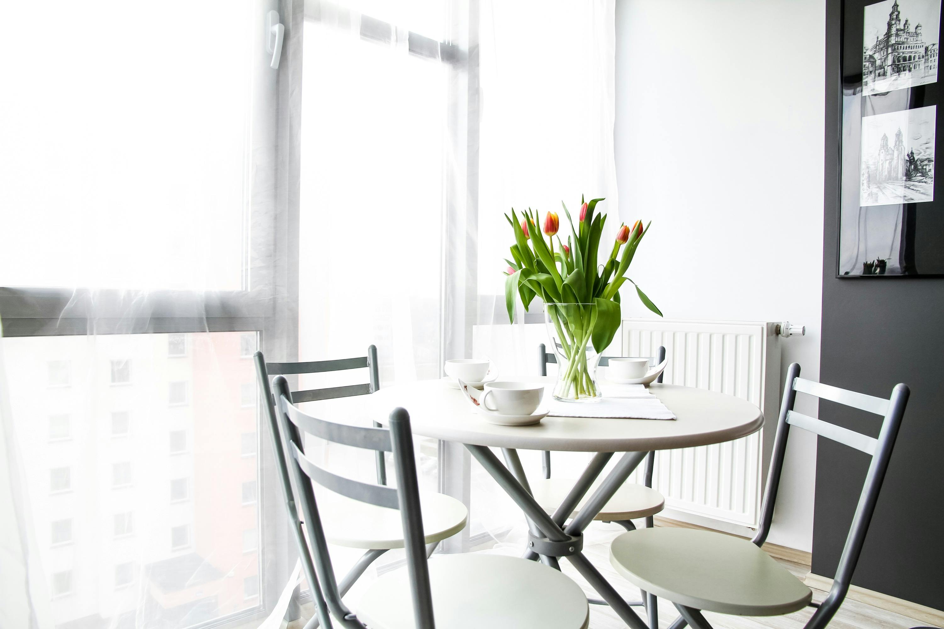 Dining area with a round table and chairs, featuring a vase of tulips.